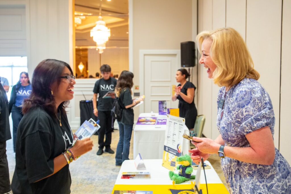 Two women standing on either side of a table holding college promotional materials